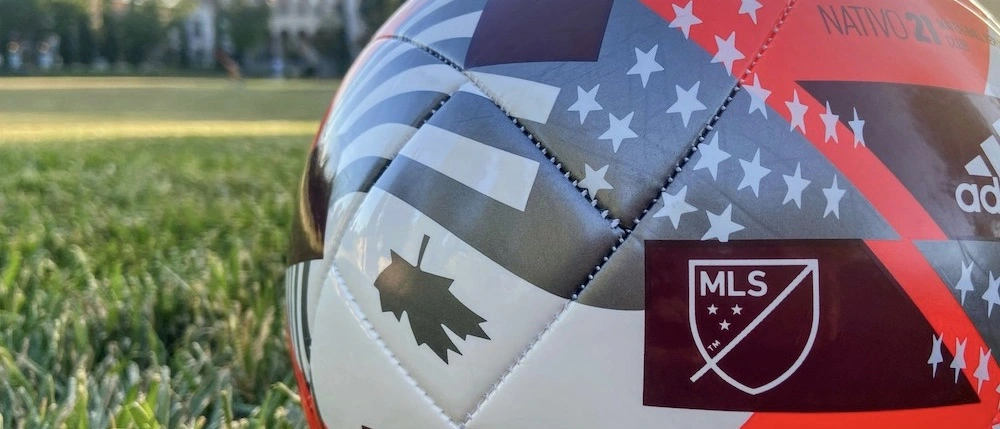 Een voetbal met MLS-logo en de vlaggen van Canada en de VS, op een voetbalveld